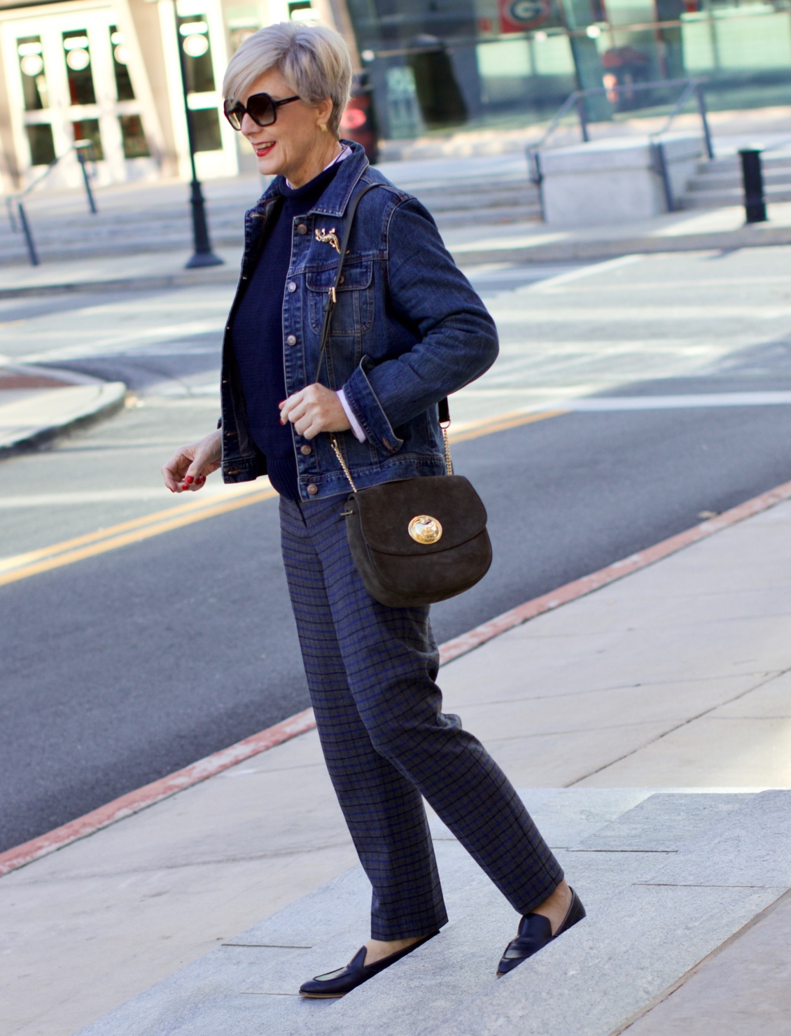beth from style at a certain age wears a jean jacket, plaid pants, navy blue roll neck sweater, striped shirt, and navy blue loafers