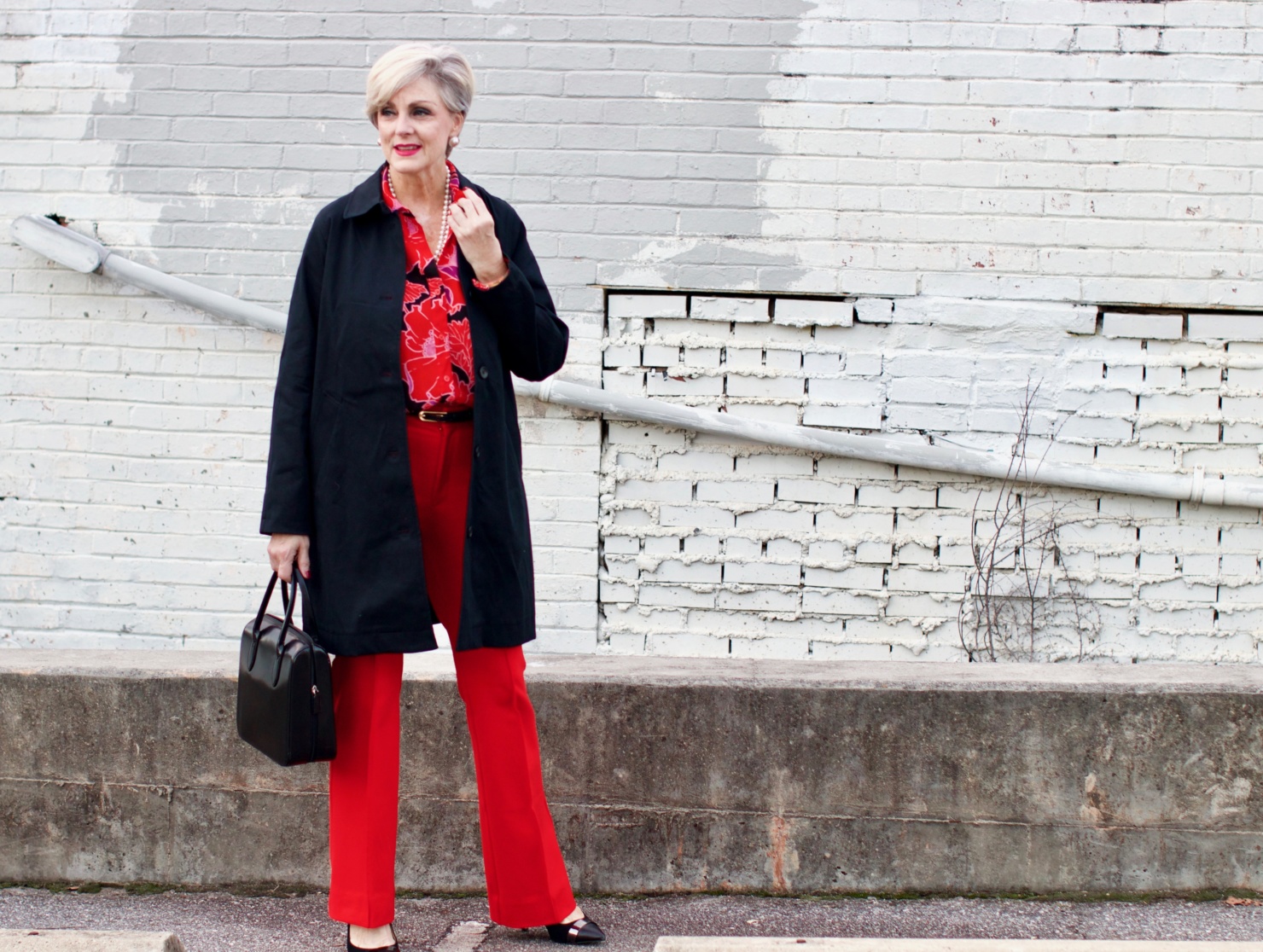 beth from Style at a Certain Age wears Anthropologie red pants, pink and red shirt, Everlane black raincoat, and black suede pumps