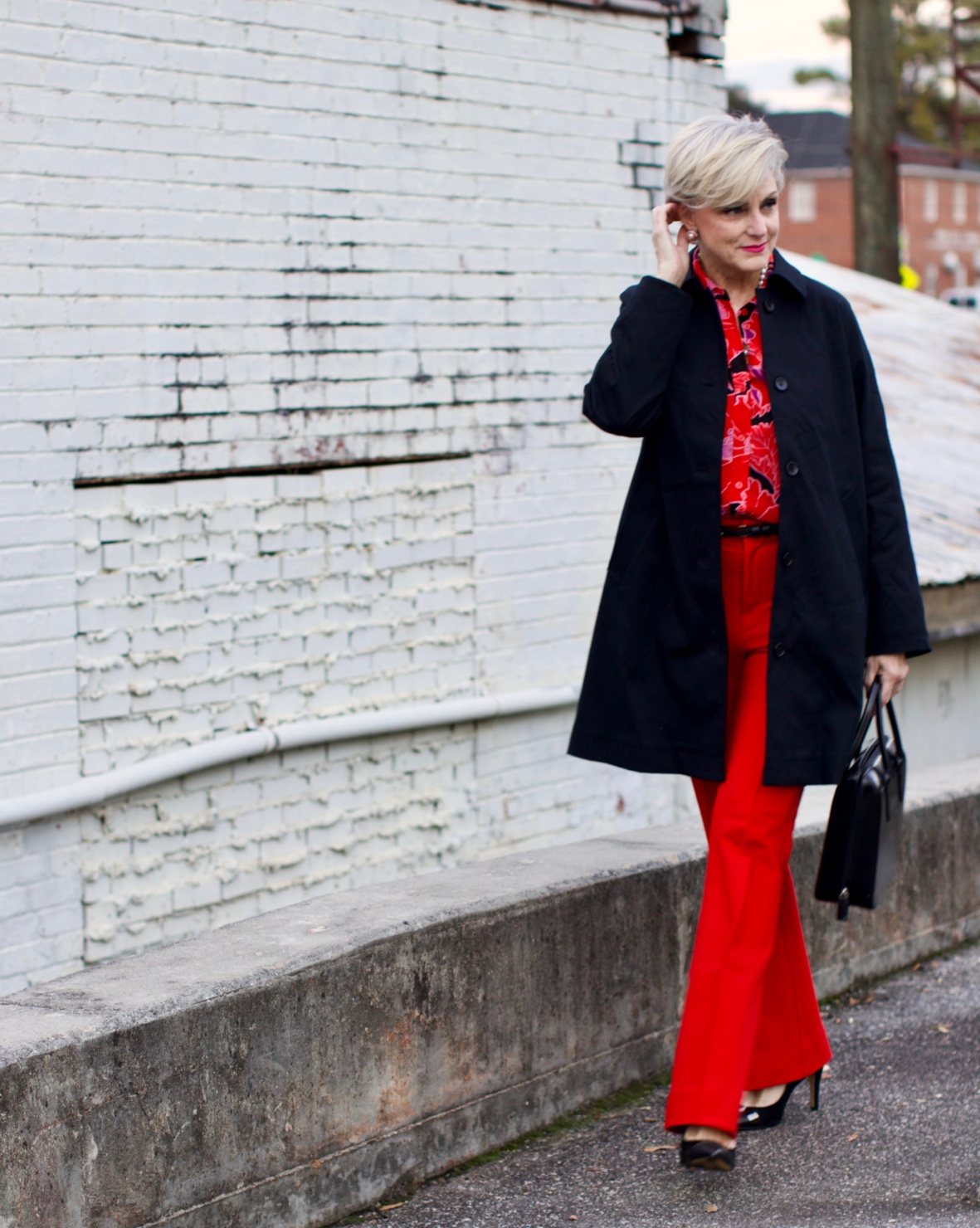 beth from Style at a Certain Age wears Anthropologie red pants, pink and red shirt, Everlane black raincoat, and black suede pumps