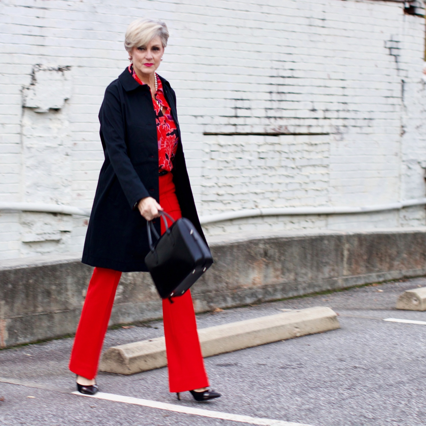beth from Style at a Certain Age wears Anthropologie red pants, pink and red shirt, Everlane black raincoat, and black suede pumps