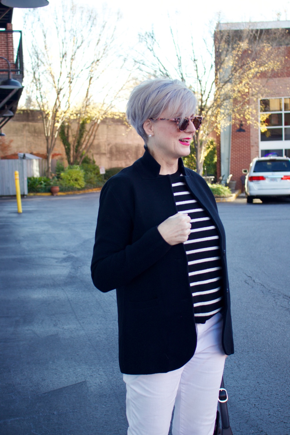 beth from Style at a Certain Age wears a red stadium coat, houndstooth cashmere scarf, white denim, striped cashmere crewneck, black ankle boots and quilted hobo handbag