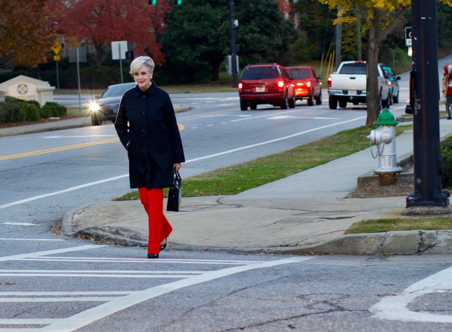 beth from Style at a Certain Age wears Anthropologie red pants, pink and red shirt, Everlane black raincoat, and black suede pumps