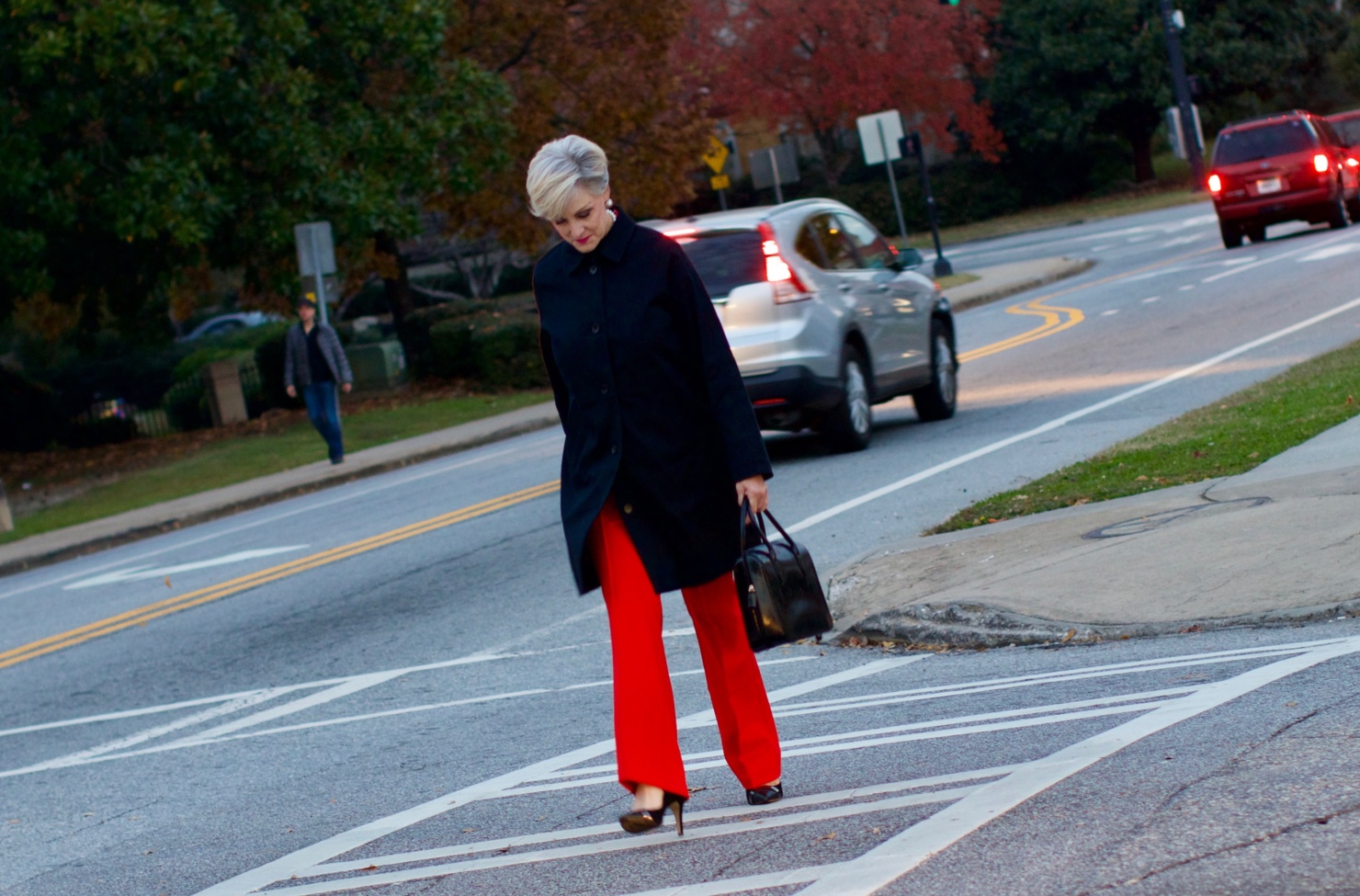 beth from Style at a Certain Age wears Anthropologie red pants, pink and red shirt, Everlane black raincoat, and black suede pumps