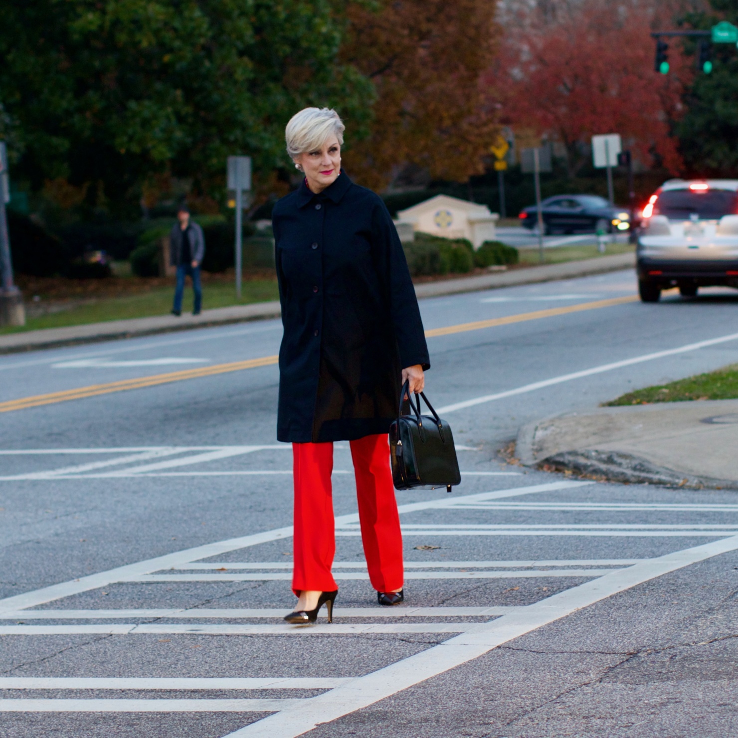beth from Style at a Certain Age wears Anthropologie red pants, pink and red shirt, Everlane black raincoat, and black suede pumps