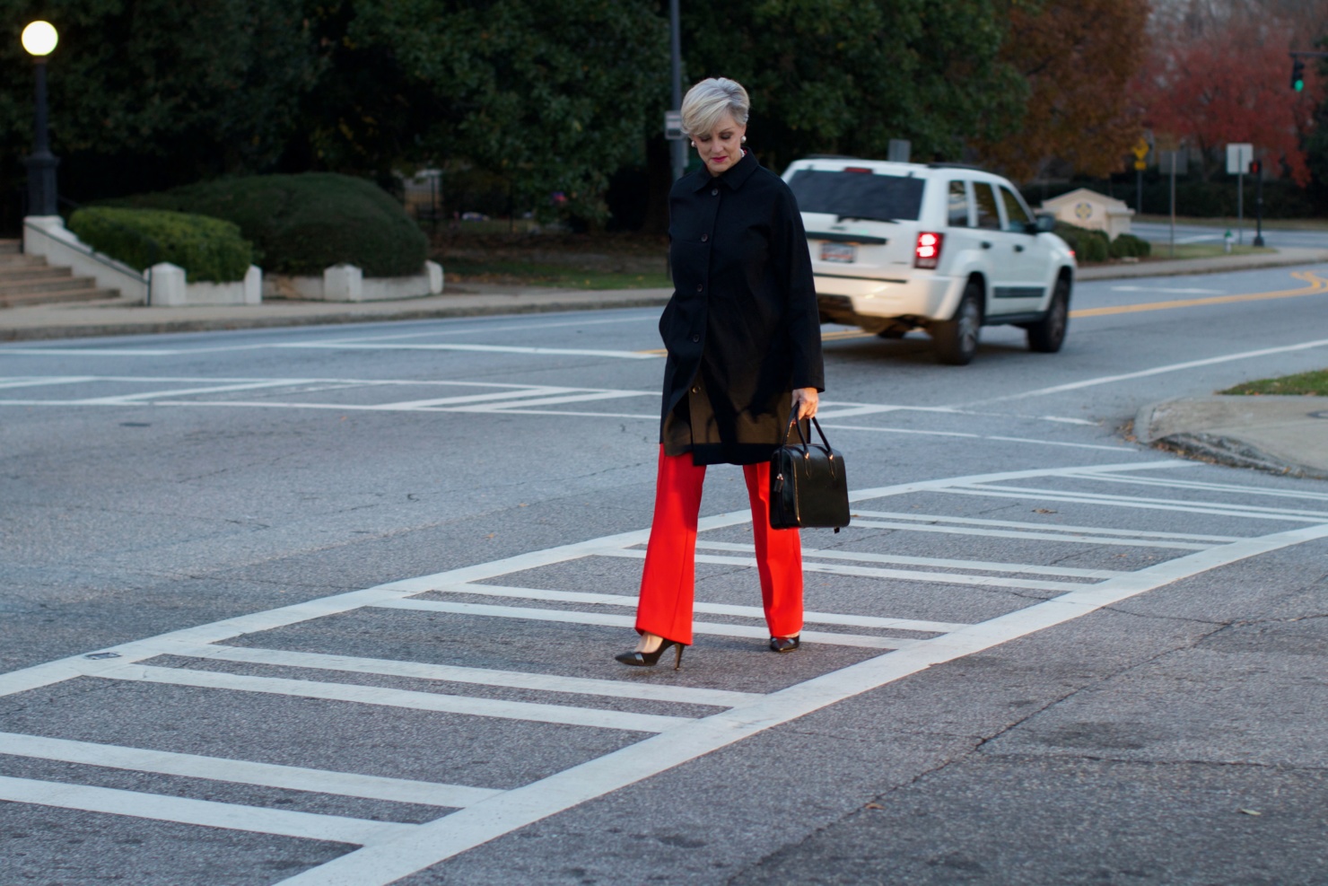 beth from Style at a Certain Age wears Anthropologie red pants, pink and red shirt, Everlane black raincoat, and black suede pumps