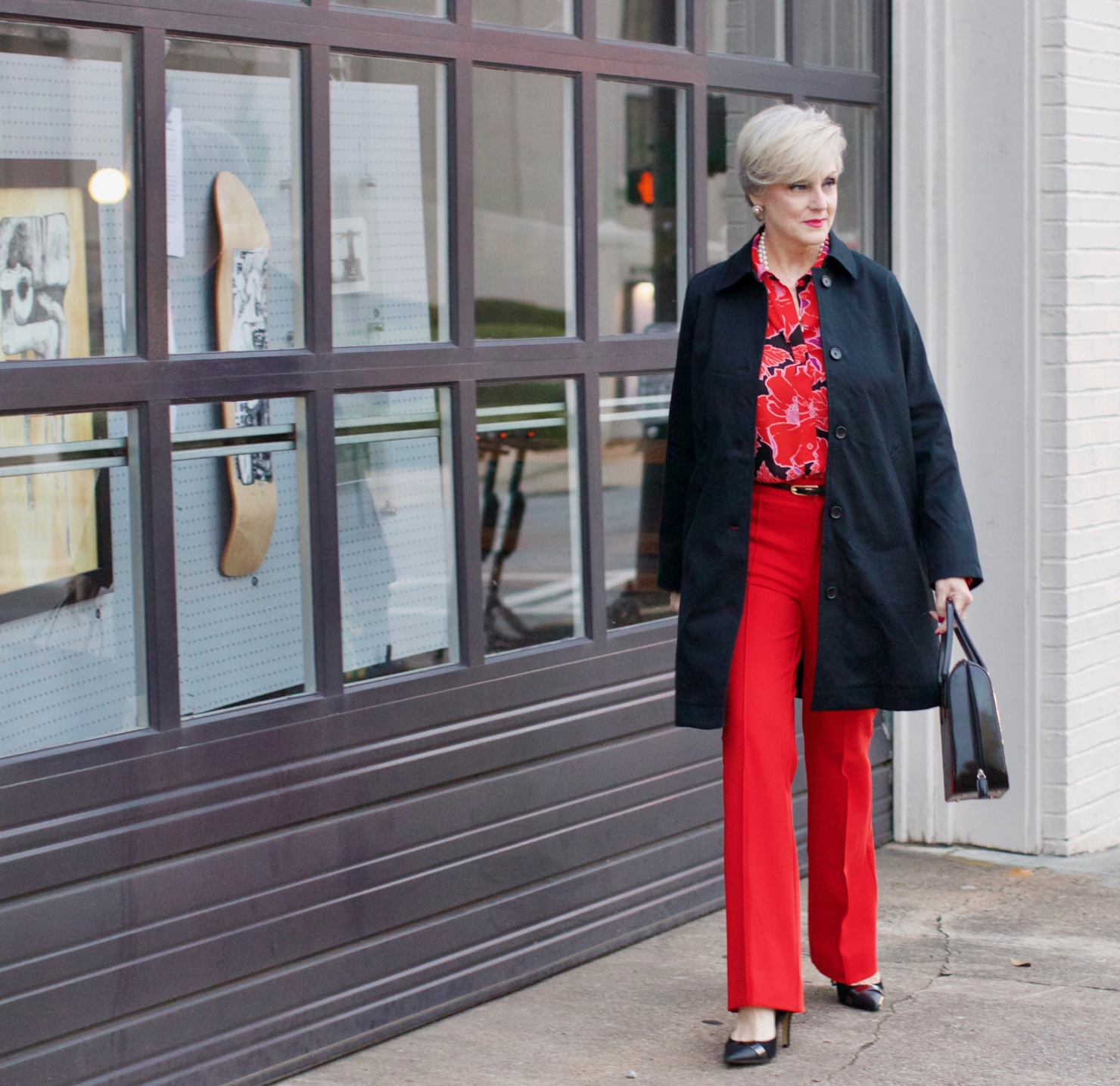 beth from Style at a Certain Age wears Anthropologie red pants, pink and red shirt, Everlane black raincoat, and black suede pumps