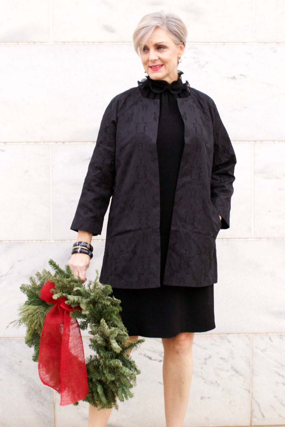 beth from Style at a Certain Age wears a Eileen Fisher shimmer jacquard 3/4 sleeve jacket and ruffled black dress 