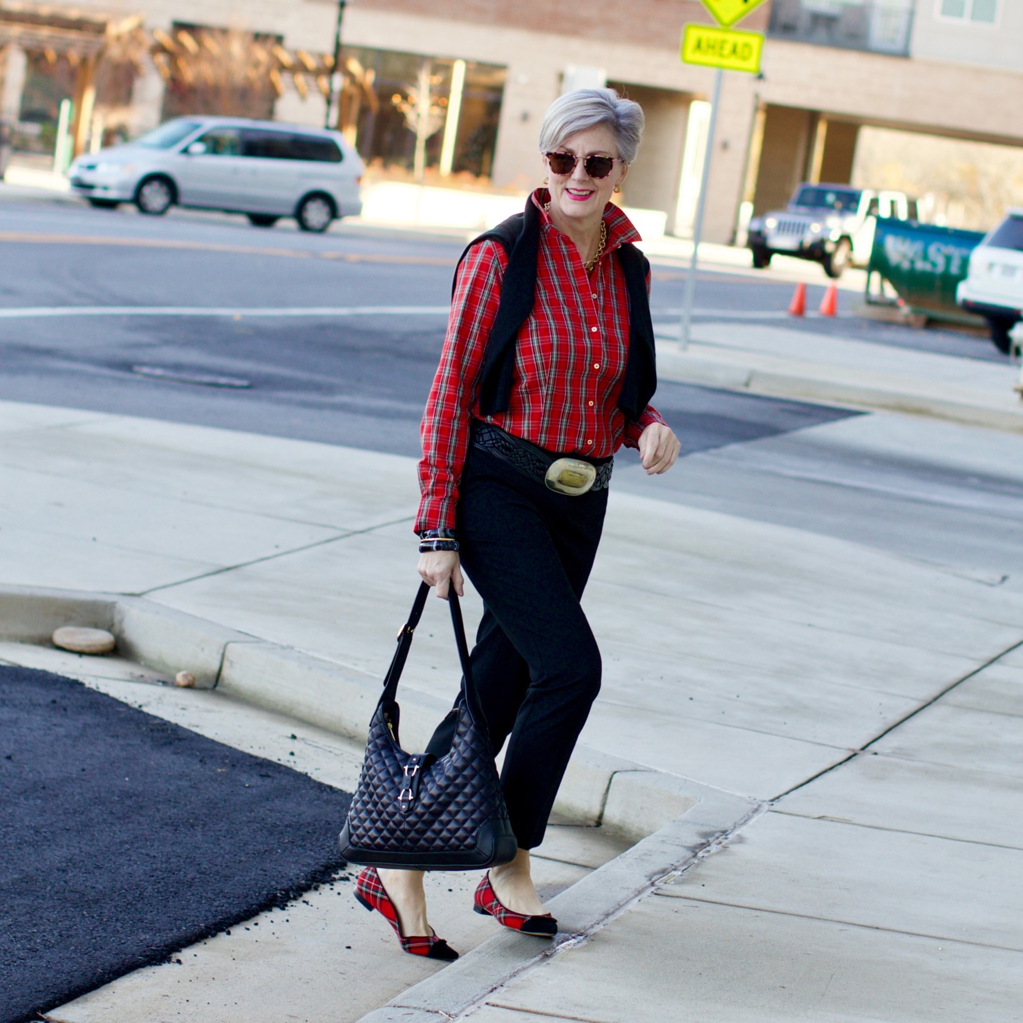 beth from Style at a Certain Age wears a tartan plaid shirt, black cropped ankle pants, tartan plaid flats, military coat and quilted hobo handbag.