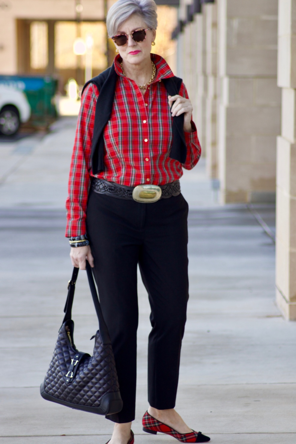 beth from Style at a Certain Age wears a tartan plaid shirt, black cropped ankle pants, tartan plaid flats, military coat and quilted hobo handbag.