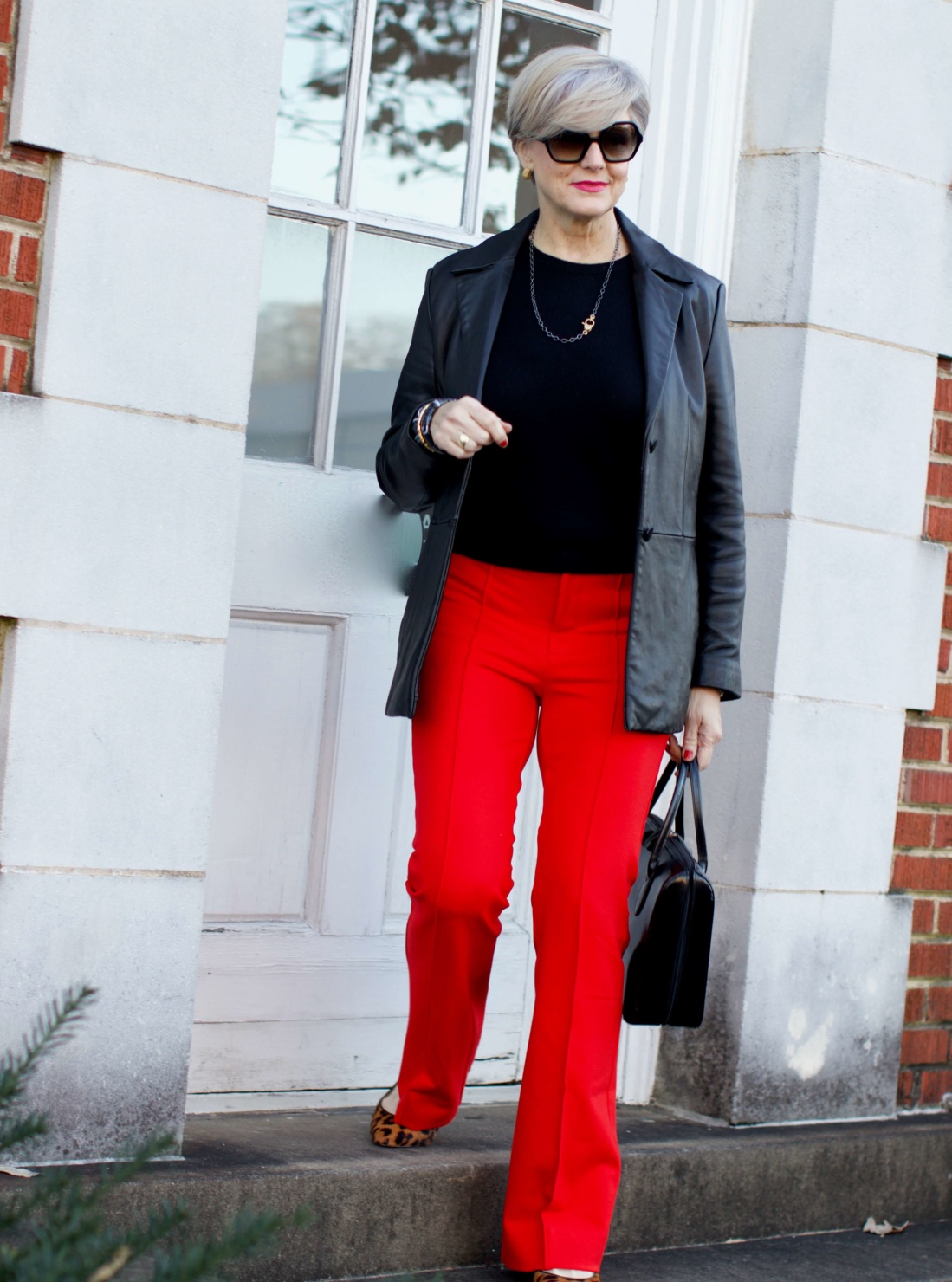 beth from Style at a Certain Age wears Anthropologie red pants, Everlane black cashmere crewneck, black leather blazer, and leopard pumps