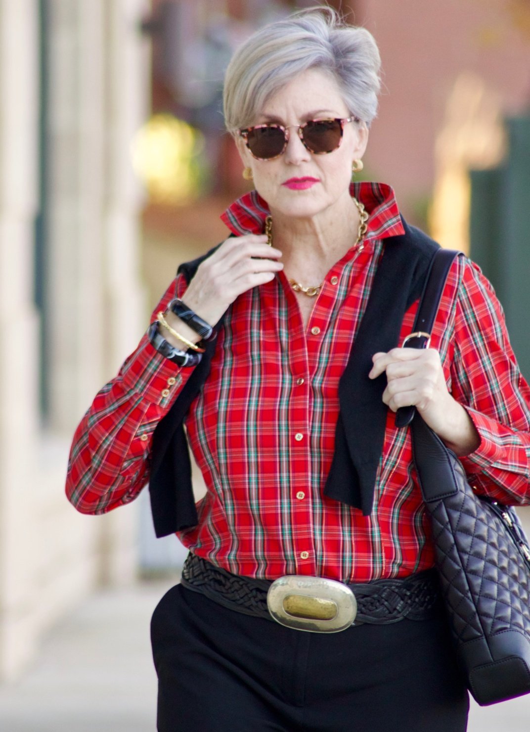 beth from Style at a Certain Age wears a tartan plaid shirt, black cropped ankle pants, tartan plaid flats, military coat and quilted hobo handbag.