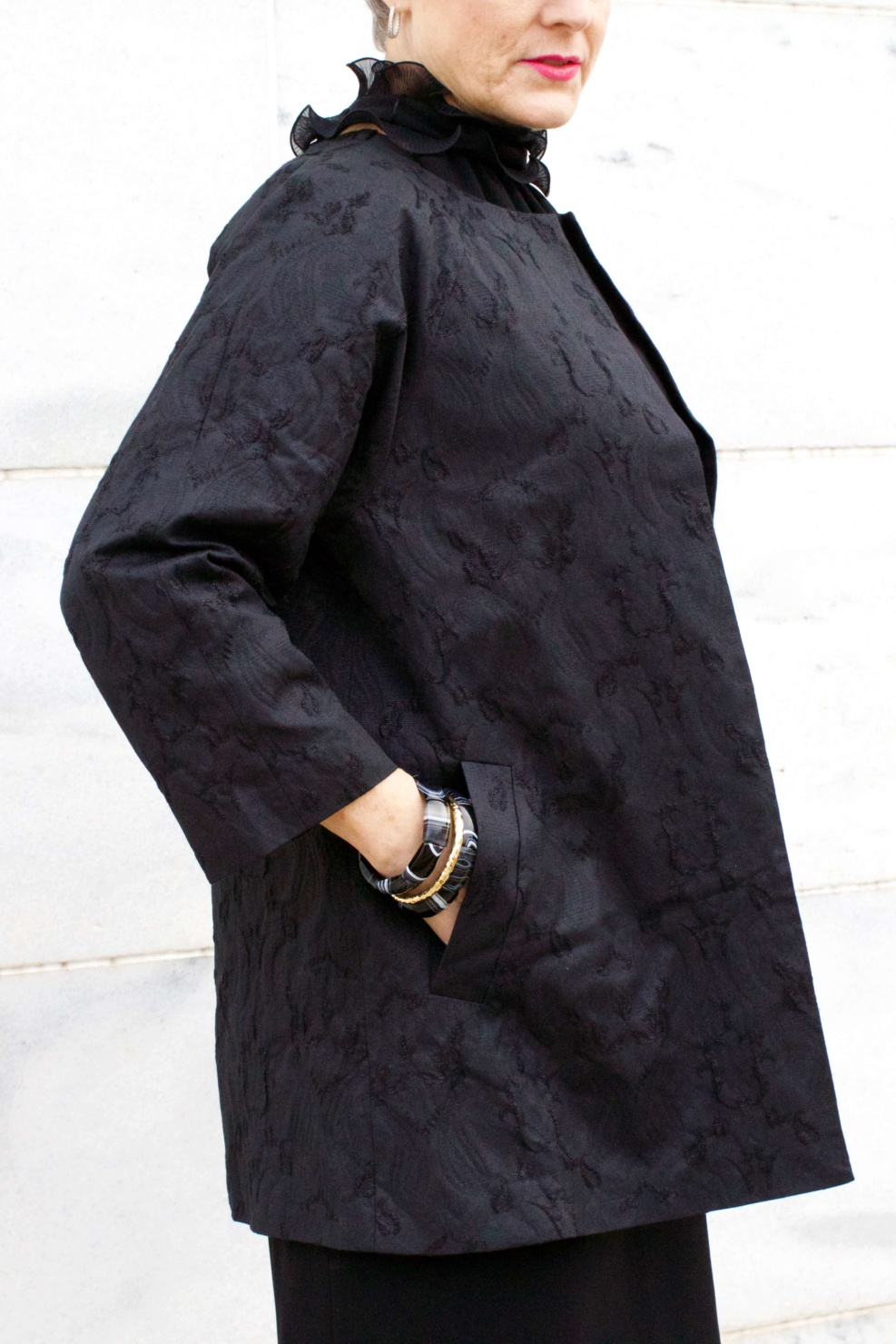 beth from Style at a Certain Age wears a Eileen Fisher shimmer jacquard 3/4 sleeve jacket and ruffled black dress 
