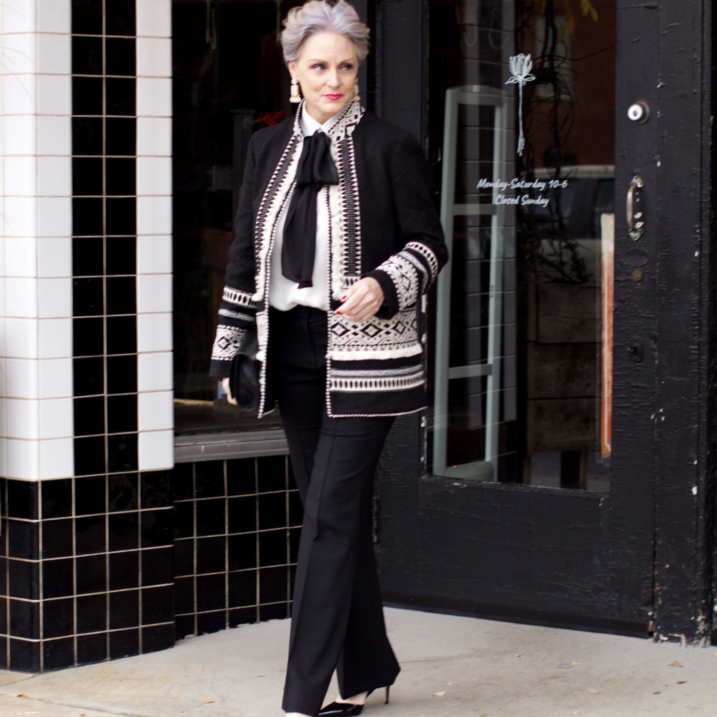 beth from Style at a Certain Age wears black flare pants, bow blouse, embroidered wonderland jacket, and black patent leather pumps