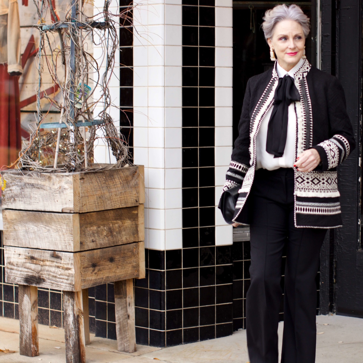 beth from Style at a Certain Age wears black flare pants, bow blouse, embroidered wonderland jacket, and black patent leather pumps