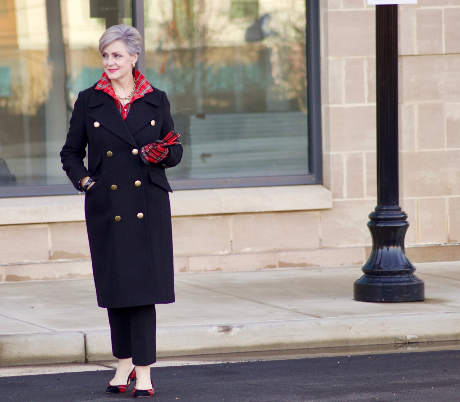 beth from Style at a Certain Age wears a tartan plaid shirt, black cropped ankle pants, tartan plaid flats, military coat and quilted hobo handbag.