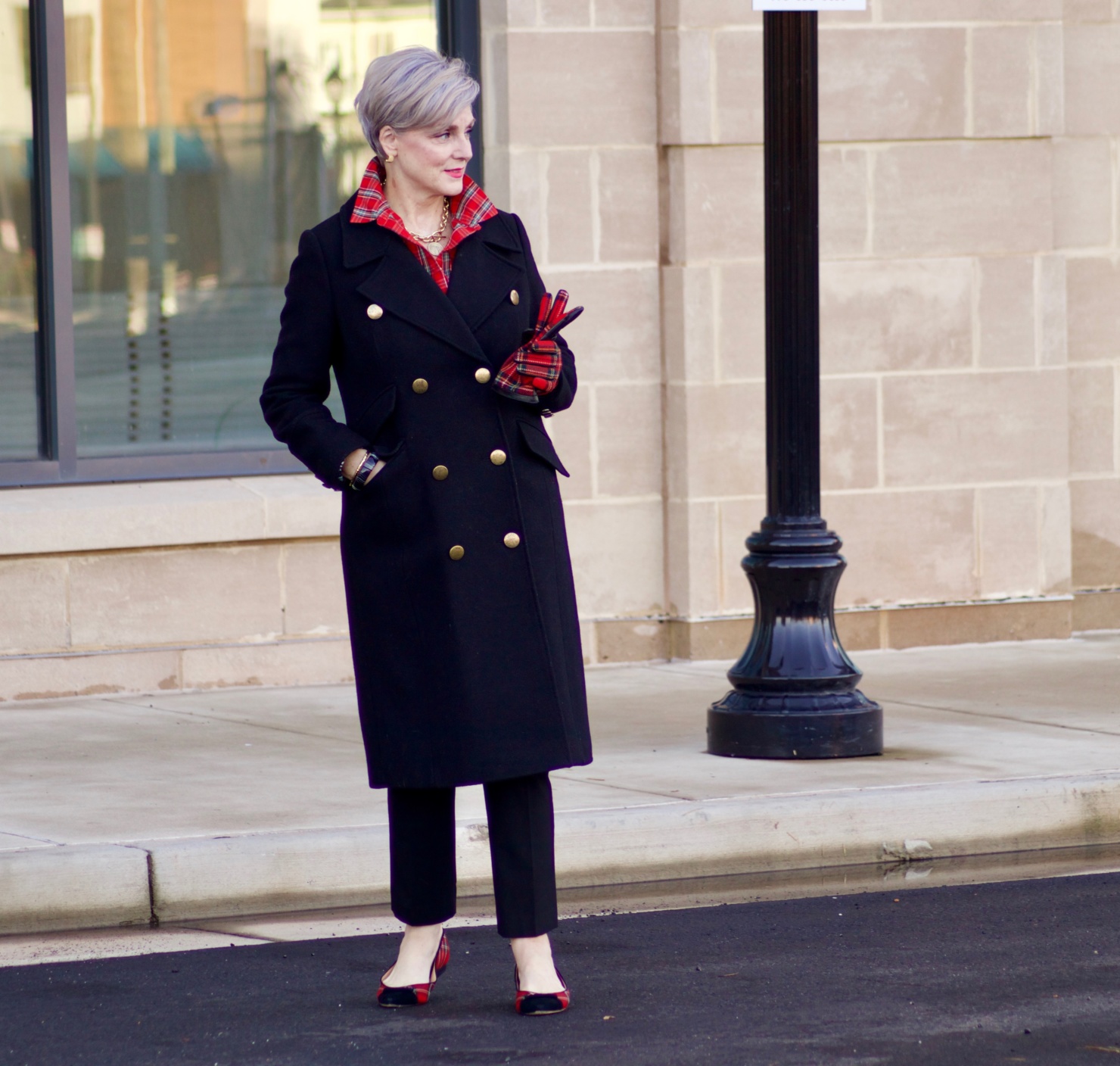 beth from Style at a Certain Age wears a tartan plaid shirt, black cropped ankle pants, tartan plaid flats, military coat and quilted hobo handbag.