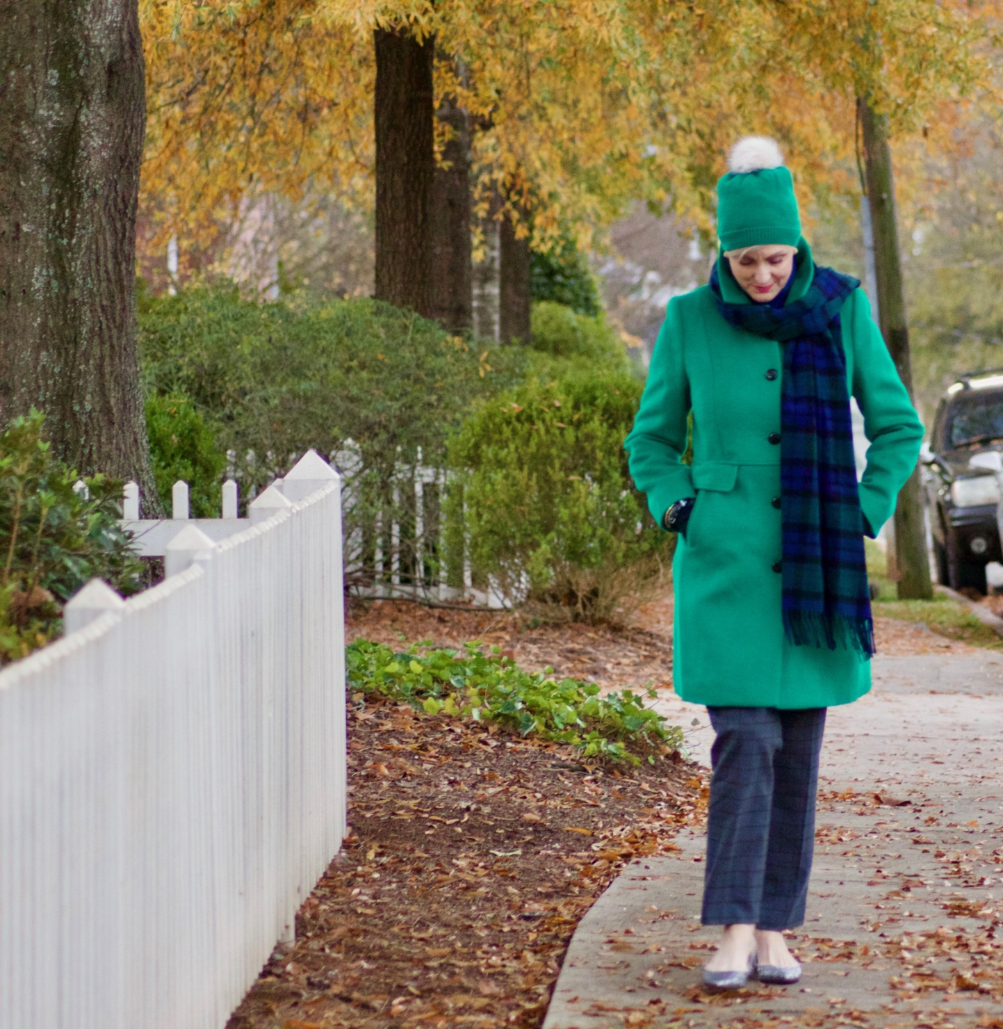 beth from style at a certain age wears plaid pants, cobalt blue turtleneck, green wool coat, blackwatch plaid cashmere scarf, and green beanie