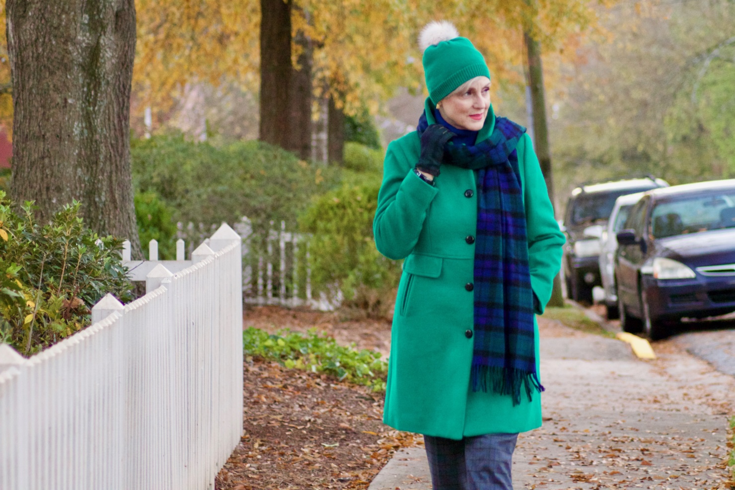 beth from style at a certain age wears plaid pants, cobalt blue turtleneck, green wool coat, blackwatch plaid cashmere scarf, and green beanie