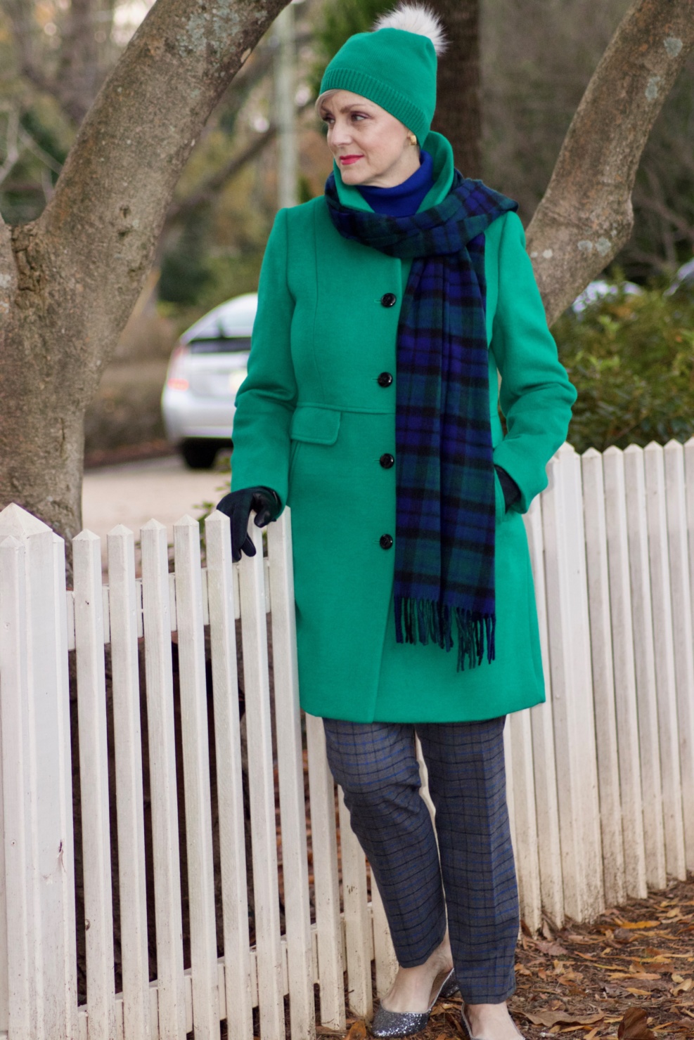 beth from style at a certain age wears plaid pants, cobalt blue turtleneck, green wool coat, blackwatch plaid cashmere scarf, and green beanie