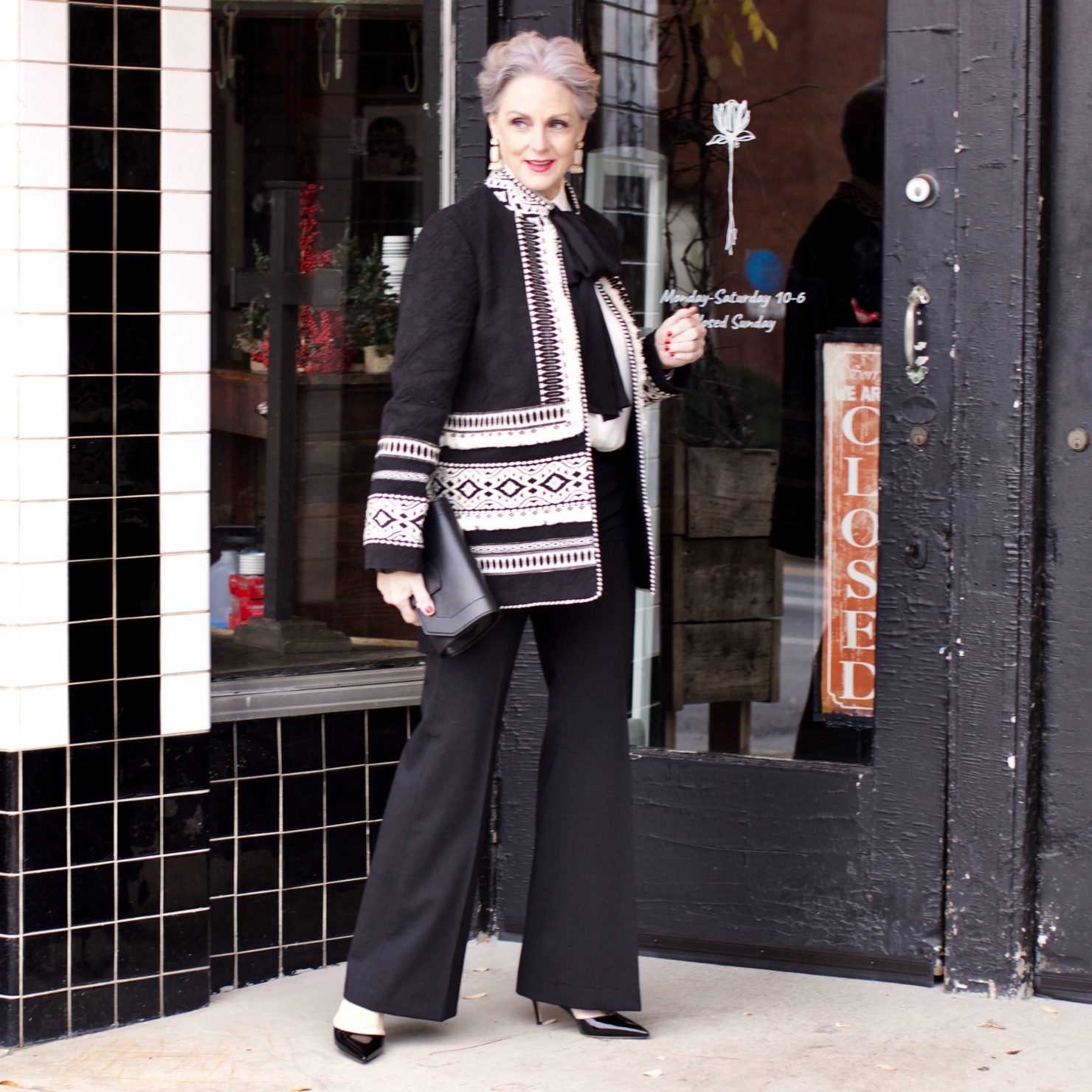 beth from Style at a Certain Age wears black flare pants, bow blouse, embroidered wonderland jacket, and black patent leather pumps