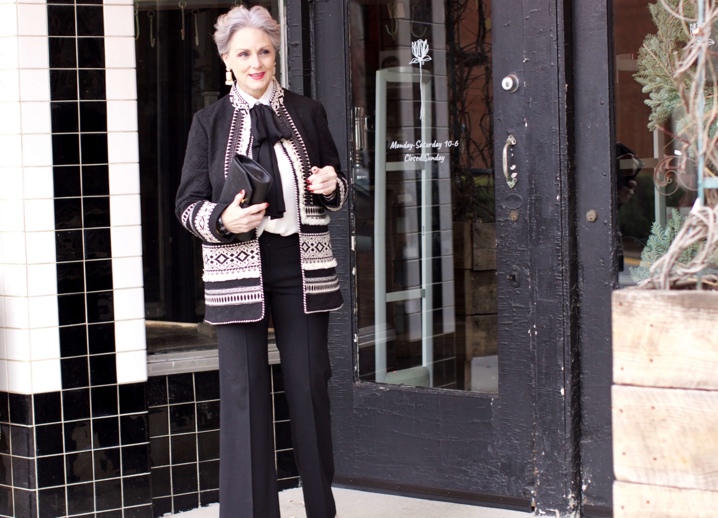 beth from Style at a Certain Age wears black flare pants, bow blouse, embroidered wonderland jacket, and black patent leather pumps