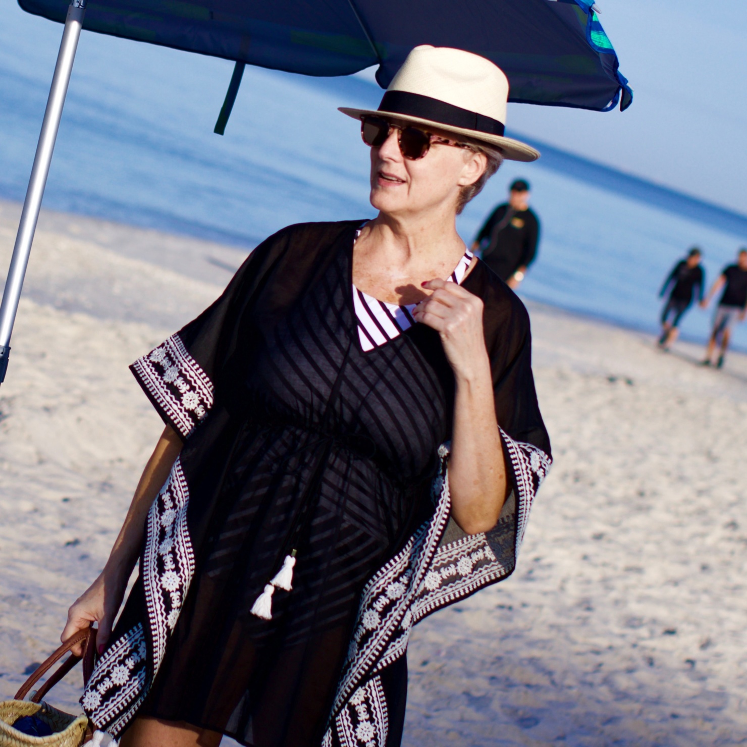 beth from Style at a Certain Age wears beach essentials, Ralph Lauren striped one-piece swimsuit, Tory Burch cover-up, jelly flip-flops, panama hat, and straw tote