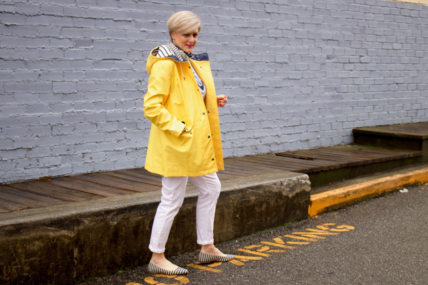 beth from Style at a Certain Age wears a yellow slicker from Talbots, white denim, anchor sweater, polka dot and striped scarf, and striped flats