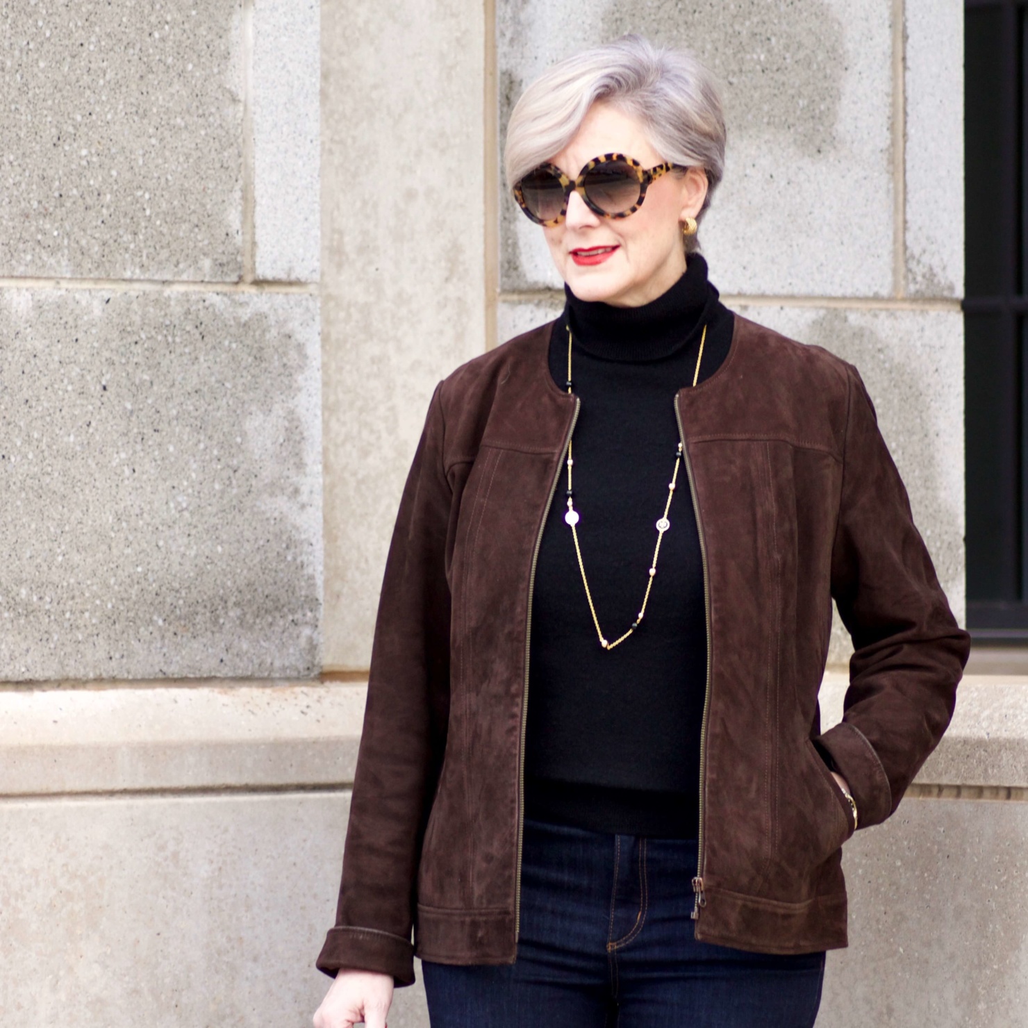 beth from Style at a Certain Age wears a black turtleneck, brown suede jacket, dark rinse denim and suede riding boots