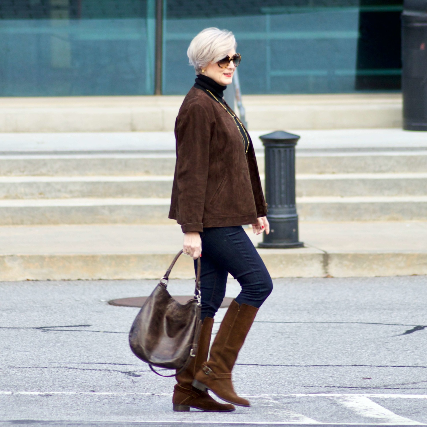 beth from Style at a Certain Age wears a black turtleneck, brown suede jacket, dark rinse denim and suede riding boots