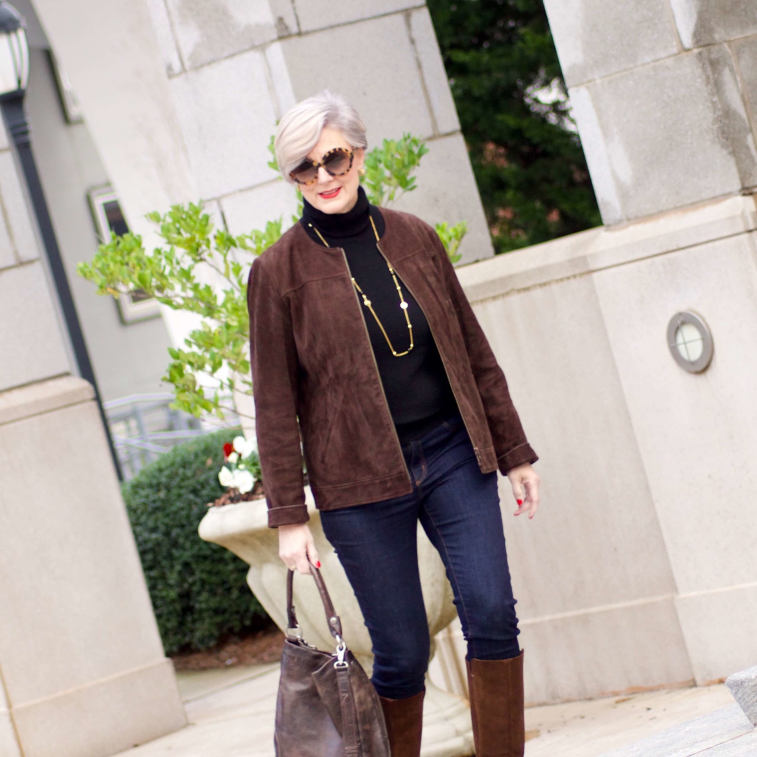 beth from Style at a Certain Age wears a black turtleneck, brown suede jacket, dark rinse denim and suede riding boots