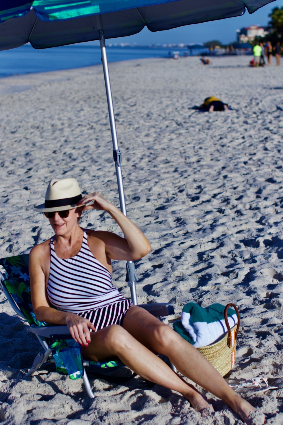 beth from Style at a Certain Age wears beach essentials, Ralph Lauren striped one-piece swimsuit, Tory Burch cover-up, jelly flip-flops, panama hat, and straw tote