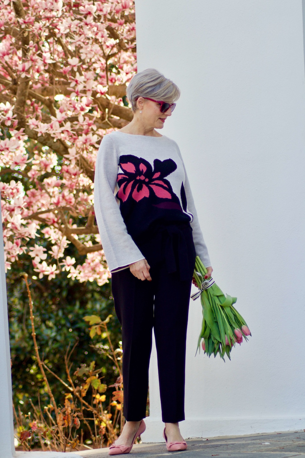 beth from Style at a Certain Age wears an Ann Taylor floral sweater, black ankle tie pants, and pink kitten heels