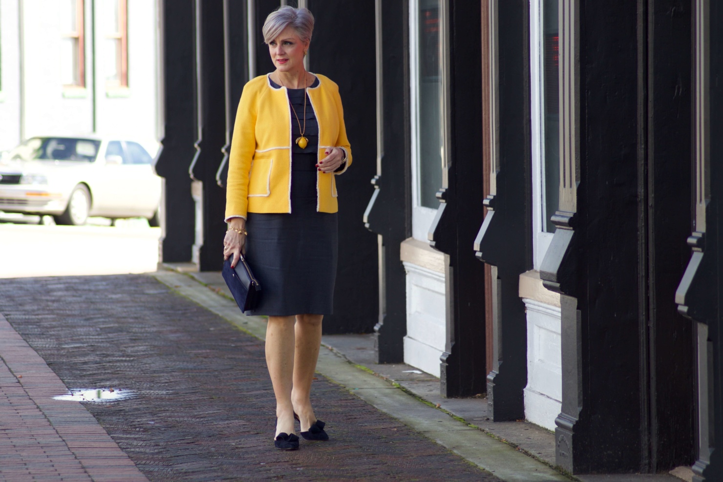 beth from Style at a Certain Age wears a navy blue sheath dress, Boden yellow jacket, navy suede shoes, Tory Burch lemon locket