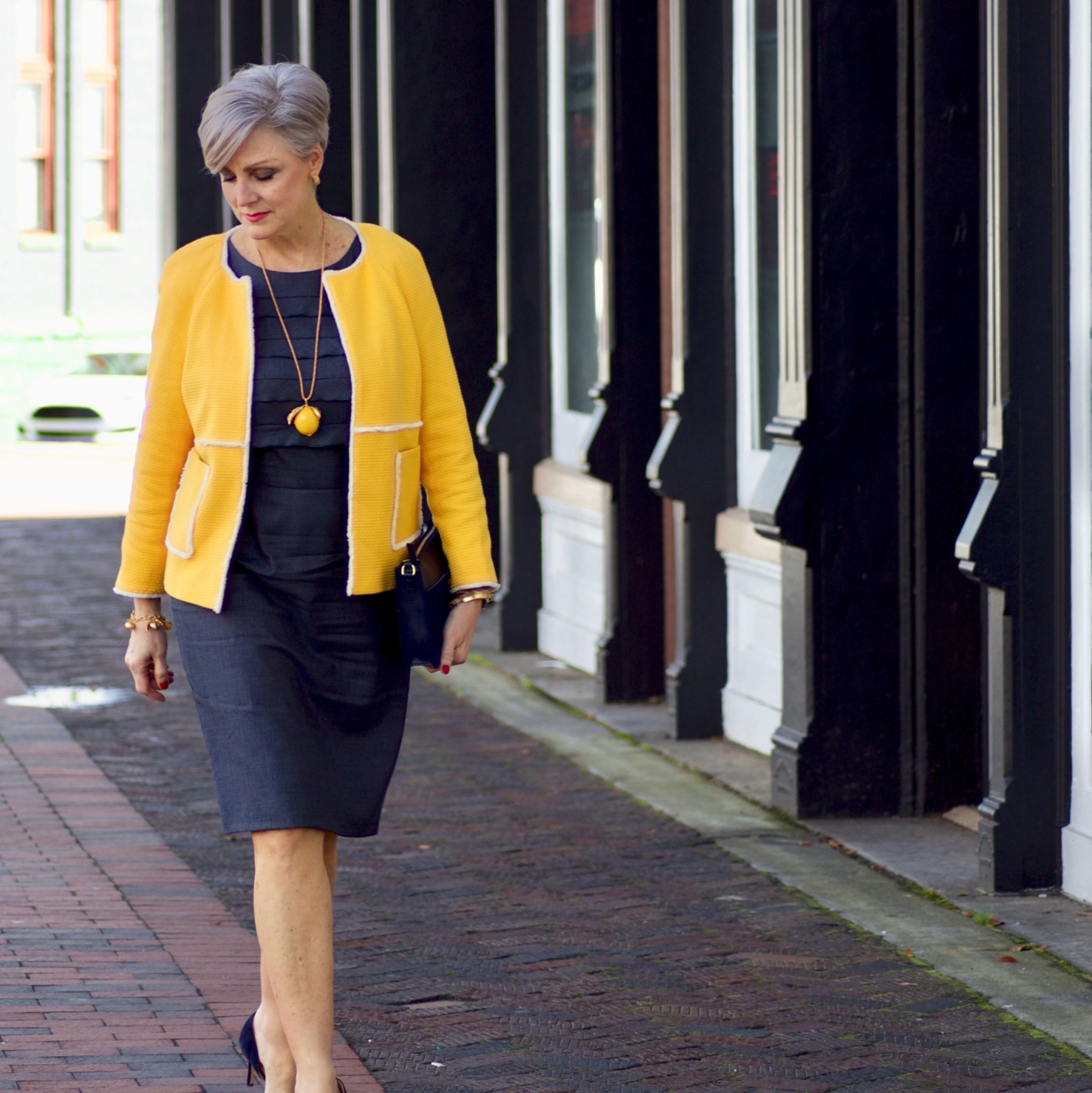 beth from Style at a Certain Age wears a navy blue sheath dress, Boden yellow jacket, navy suede shoes, Tory Burch lemon locket