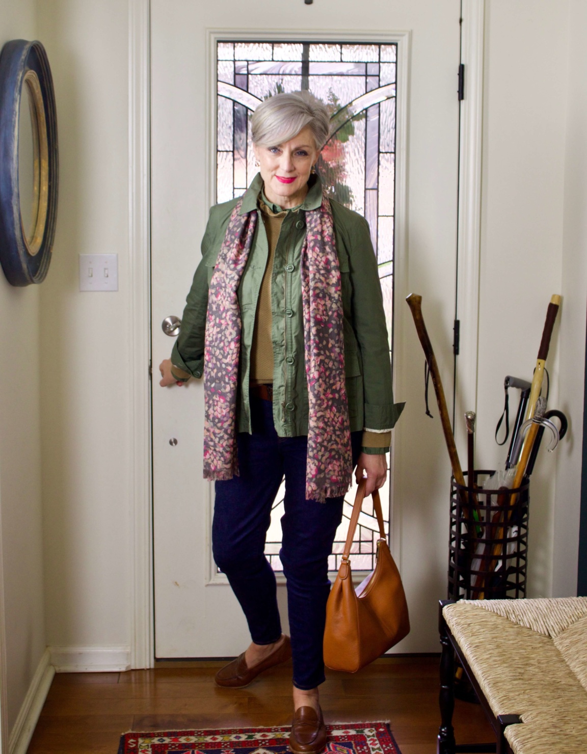 beth from Style at a Certain Age wears a ruffleneck sweater, skinny jeans, green utility jacket, hobo handbag, and loafers