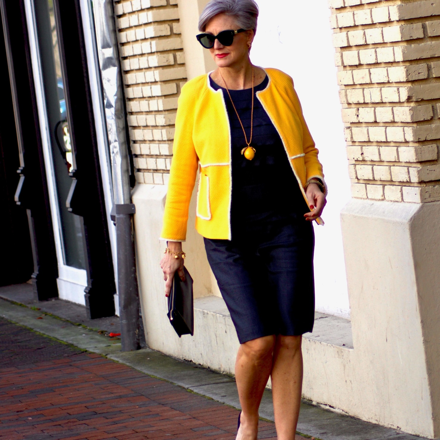 beth from Style at a Certain Age wears a navy blue sheath dress, Boden yellow jacket, navy suede shoes, Tory Burch lemon locket
