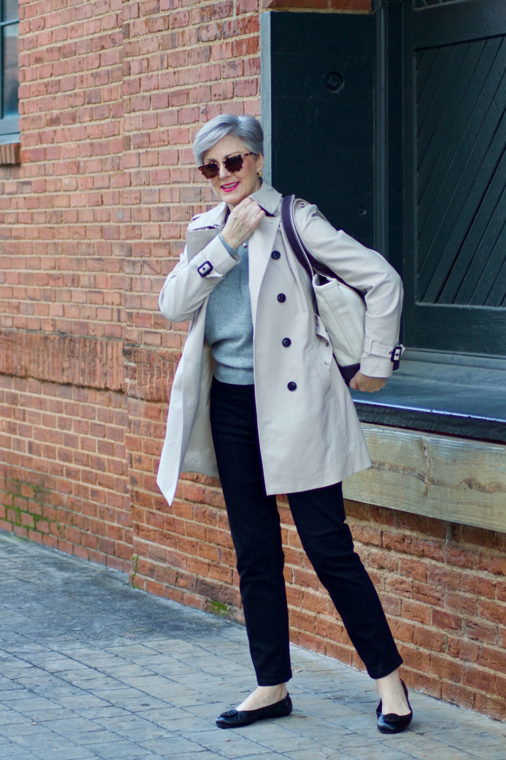 beth from Style at a Certain Age wears an Everlane grey cashmere crewneck, high rise black cigarette jean, Tory Burch black ballet flats and a double-breasted trench coat