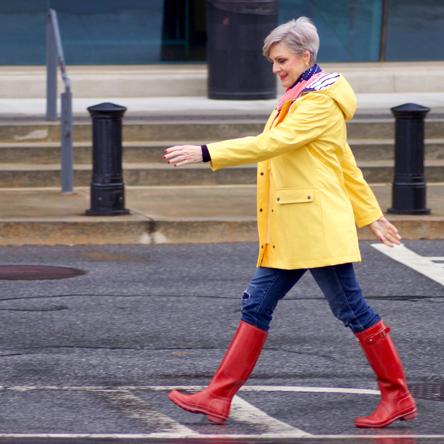 beth from Style at a Certain Age wears Hunter high gloss red rain boots, navy turtleneck, vintage straight jeans, yellow raincoat, and polka dot scarf