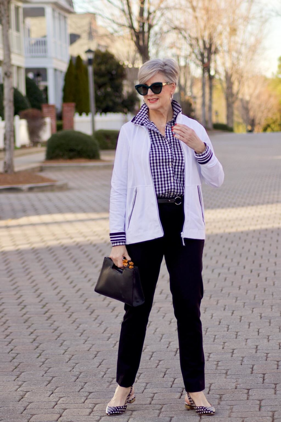 beth from Style at a Certain Age wears a gingham button up, black hampton pants, white track jacket, edison polka dot slingbacks