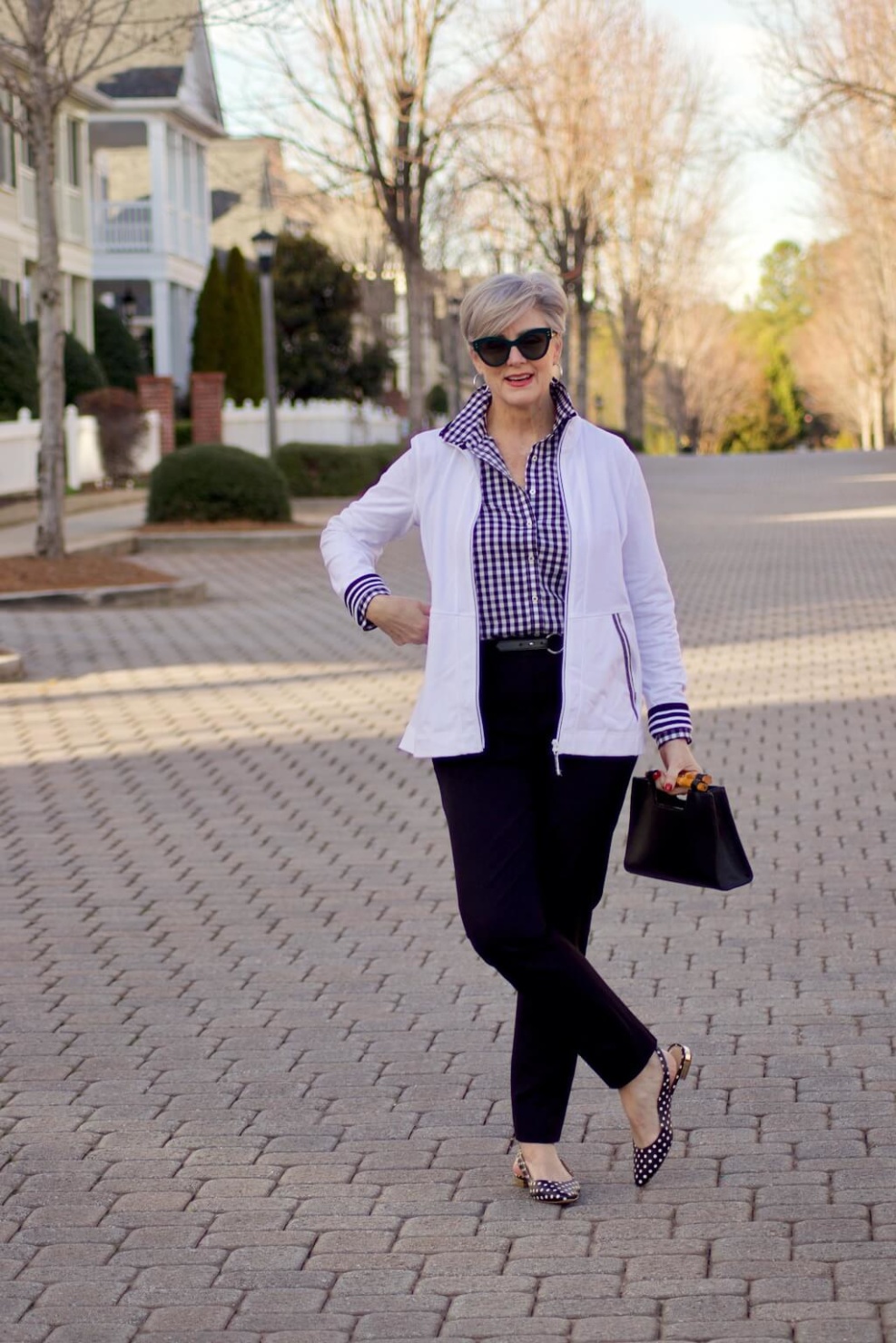 beth from Style at a Certain Age wears a gingham button up, black hampton pants, white track jacket, edison polka dot slingbacks