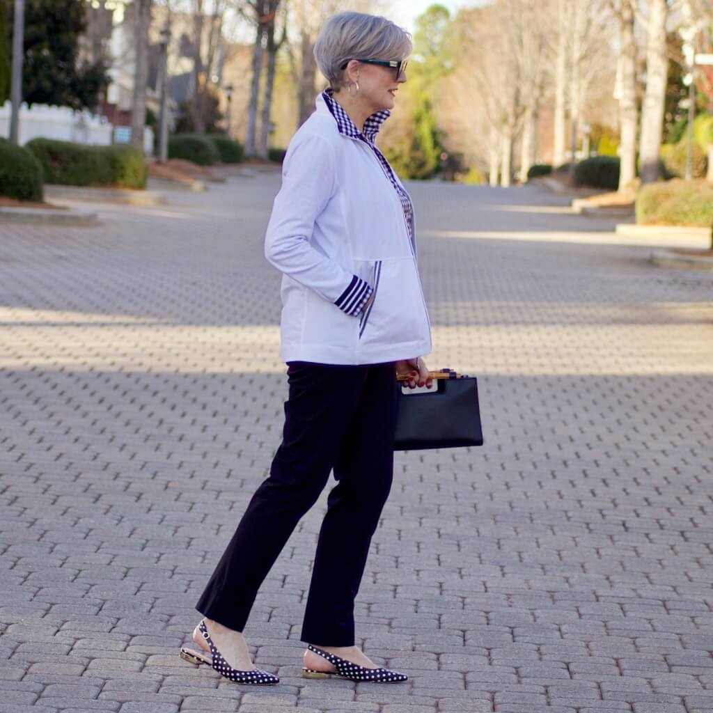 beth from Style at a Certain Age wears a gingham button up, black hampton pants, white track jacket, edison polka dot slingbacks