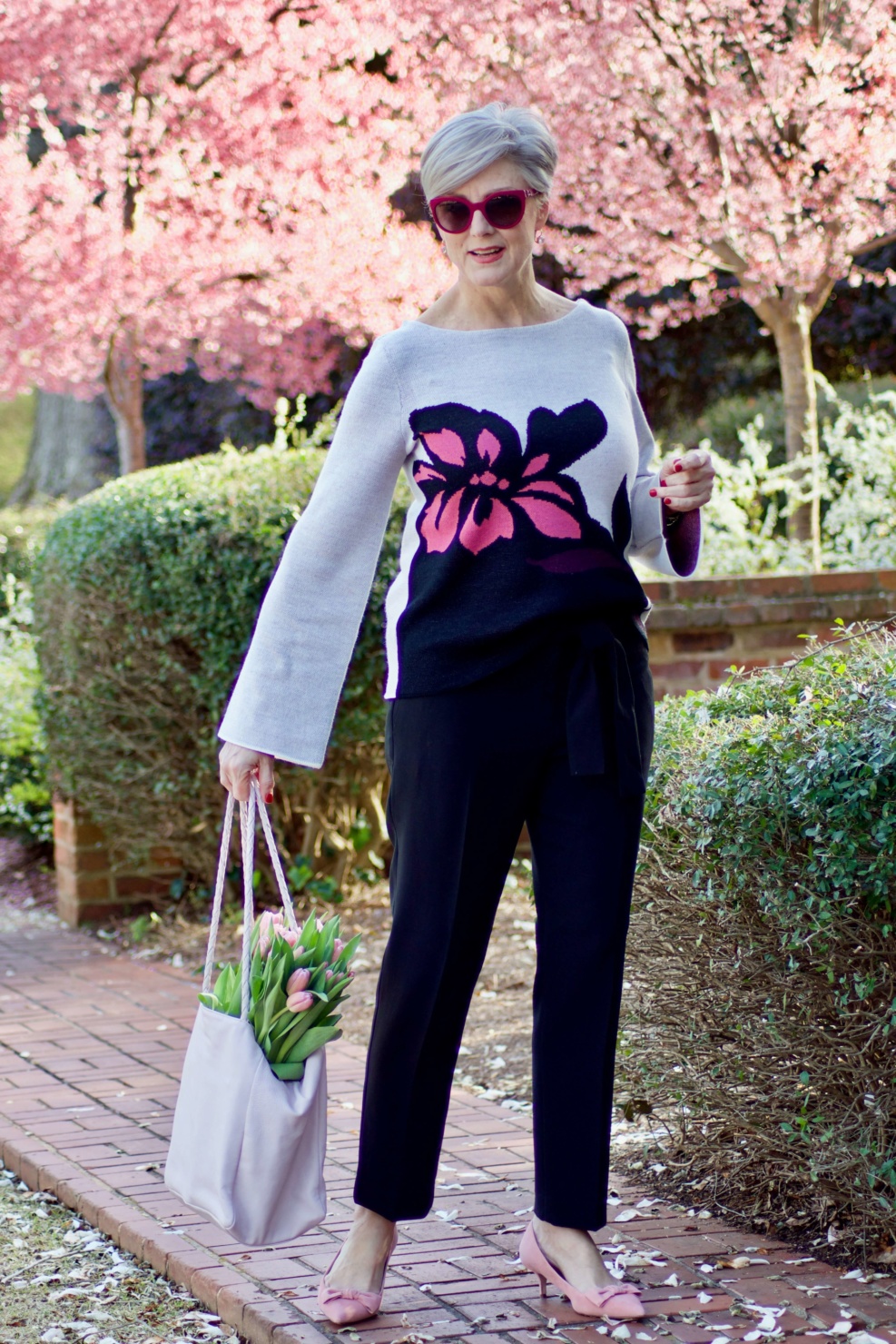beth from Style at a Certain Age wears an Ann Taylor floral sweater, black ankle tie pants, and pink kitten heels