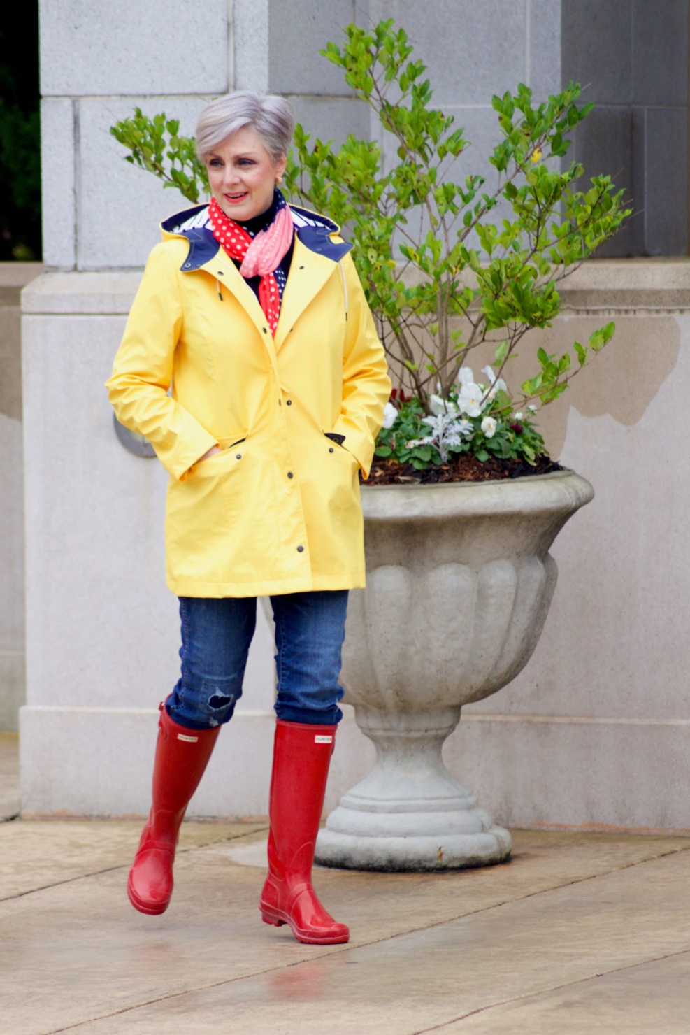beth from Style at a Certain Age wears Hunter high gloss red rain boots, navy turtleneck, vintage straight jeans, yellow raincoat, and polka dot scarf
