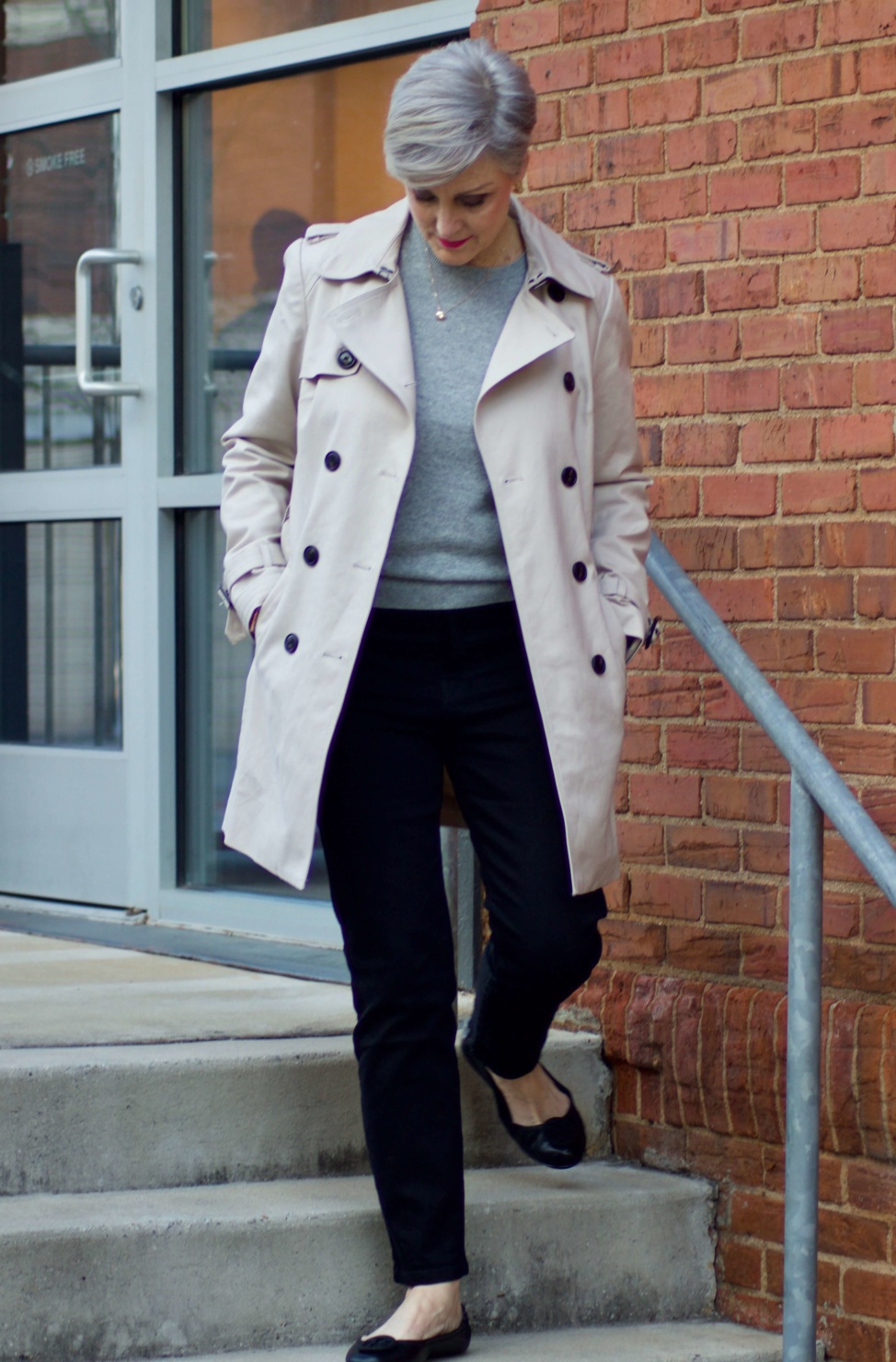 beth from Style at a Certain Age wears an Everlane grey cashmere crewneck, high rise black cigarette jean, Tory Burch black ballet flats and a double-breasted trench coat