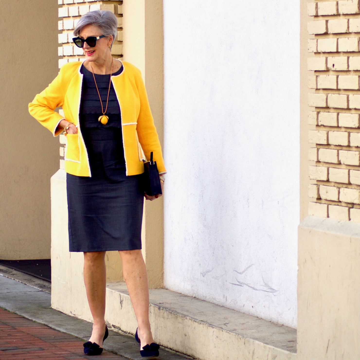 beth from Style at a Certain Age wears a navy blue sheath dress, Boden yellow jacket, navy suede shoes, Tory Burch lemon locket
