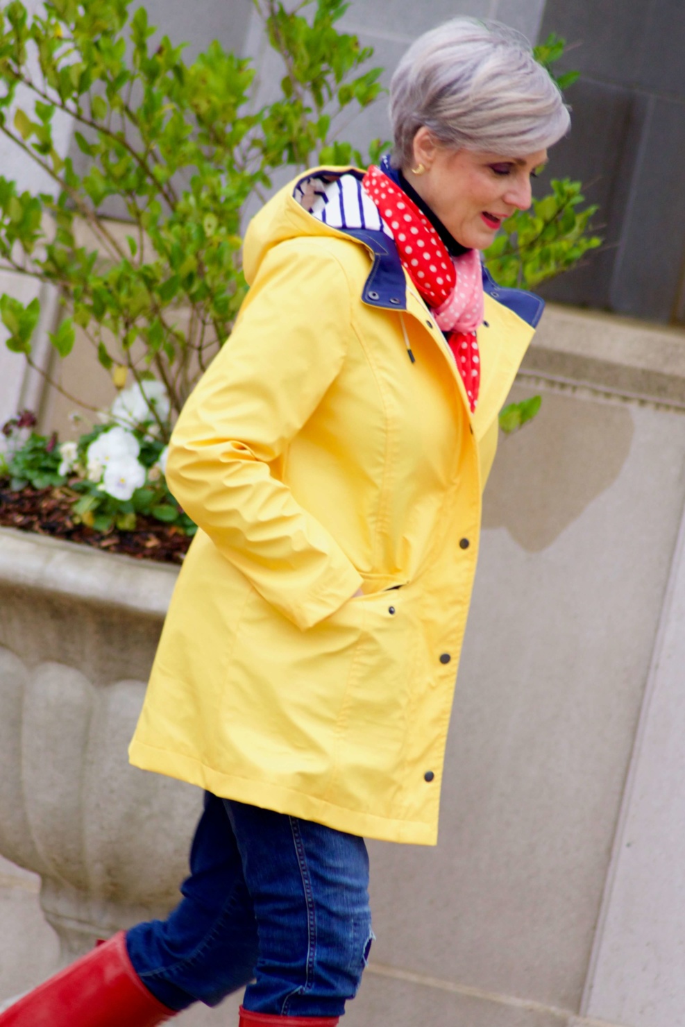beth from Style at a Certain Age wears Hunter high gloss red rain boots, navy turtleneck, vintage straight jeans, yellow raincoat, and polka dot scarf