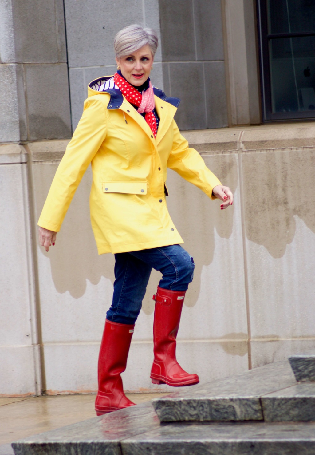beth from Style at a Certain Age wears Hunter high gloss red rain boots, navy turtleneck, vintage straight jeans, yellow raincoat, and polka dot scarf