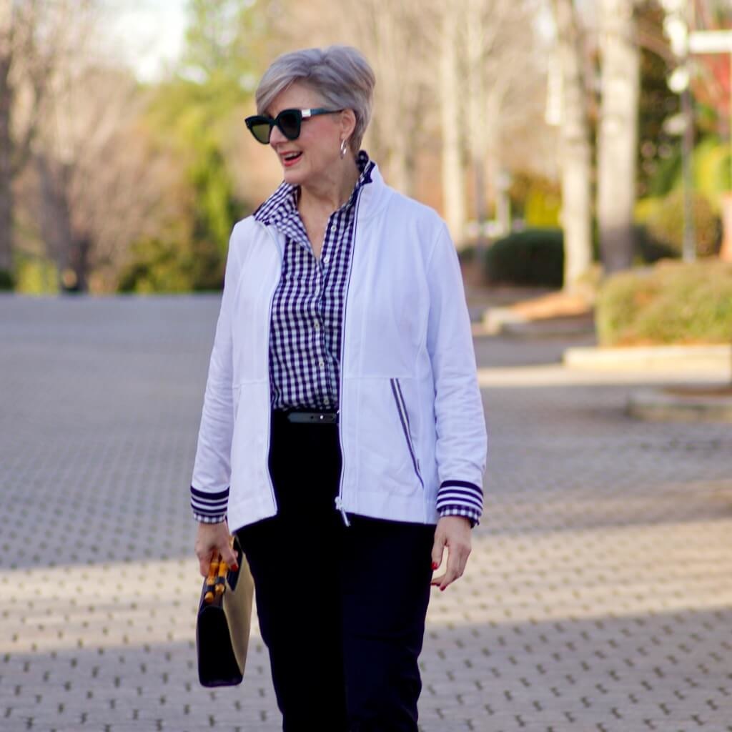 beth from Style at a Certain Age wears a gingham button up, black hampton pants, white track jacket, edison polka dot slingbacks