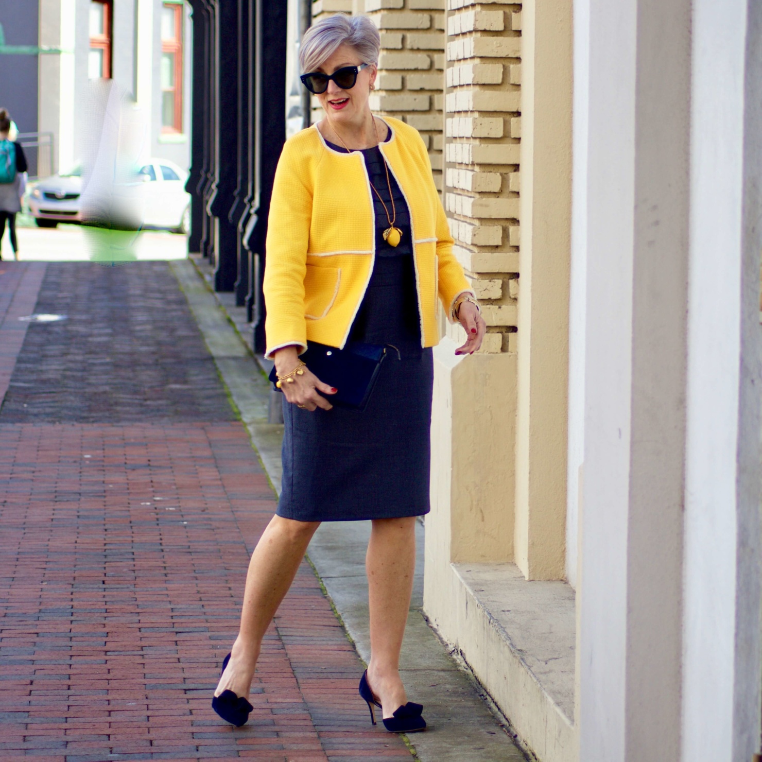 beth from Style at a Certain Age wears a navy blue sheath dress, Boden yellow jacket, navy suede shoes, Tory Burch lemon locket