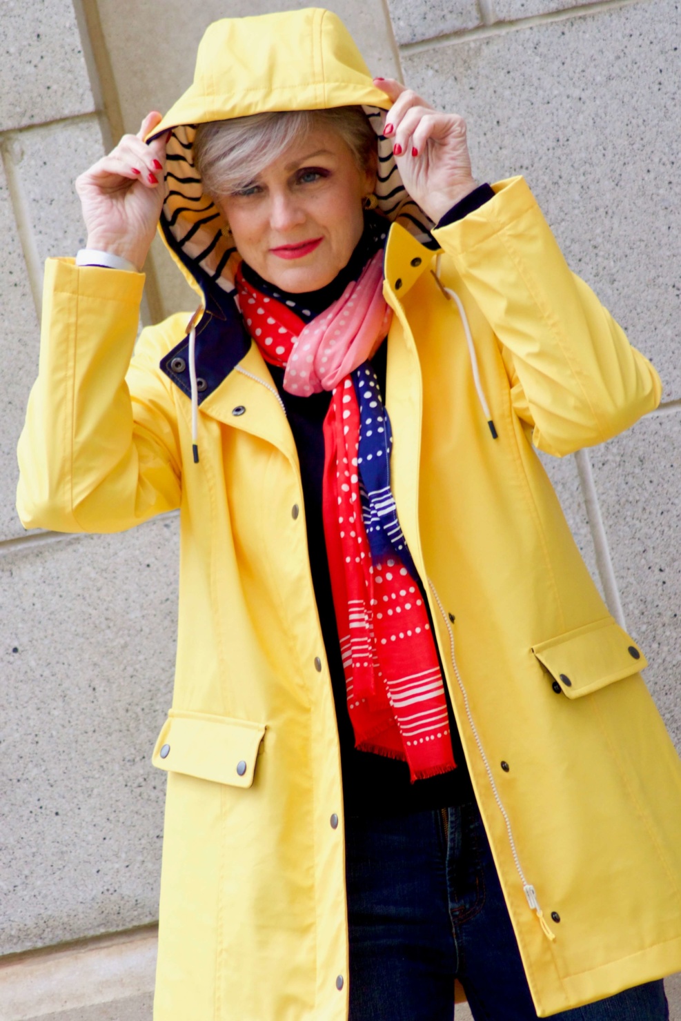 beth from Style at a Certain Age wears Hunter high gloss red rain boots, navy turtleneck, vintage straight jeans, yellow raincoat, and polka dot scarf